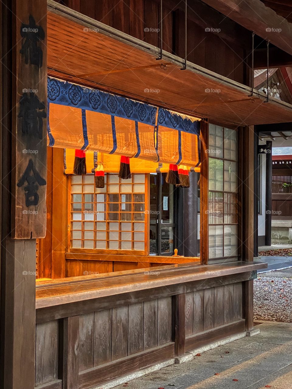 Orange and blue Japanese traditional drapes over box window at Meiji Jingu shrine, with warm orange glow lighting up the wooden building.