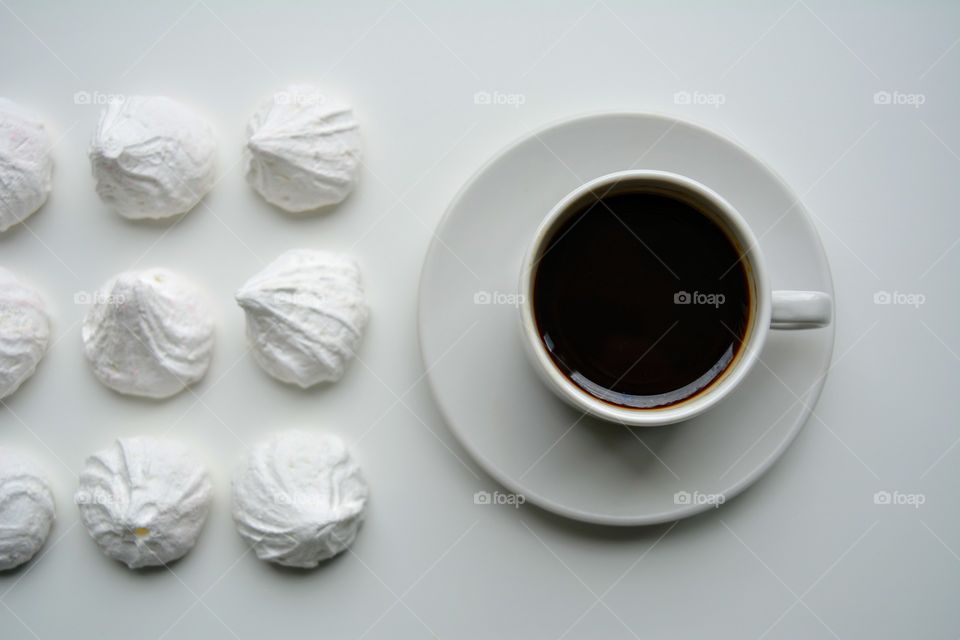 cup of coffee and sweet sugar meringues on a white background, beautiful texture top view