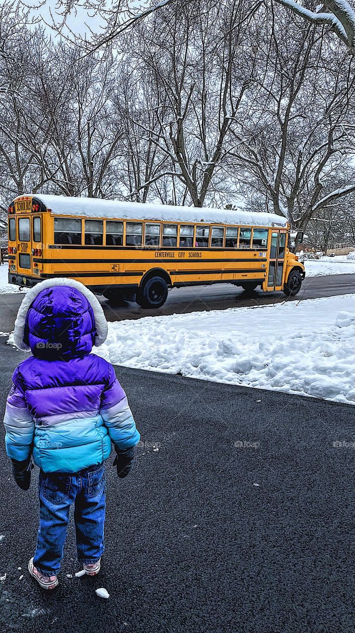 Toddler girl watches bus go by, toddler loves school buses, waiting for the bus, children and school buses, school bus in the snow 