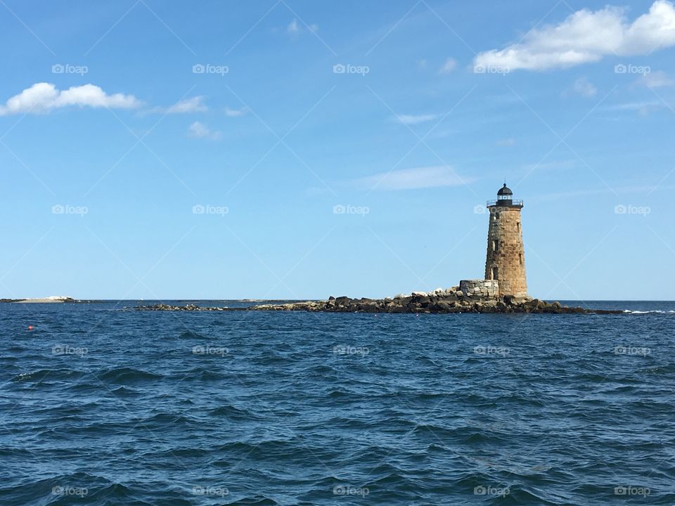 Picturesque view of a New England lighthouse out on the water. Bright summer day out on the sea