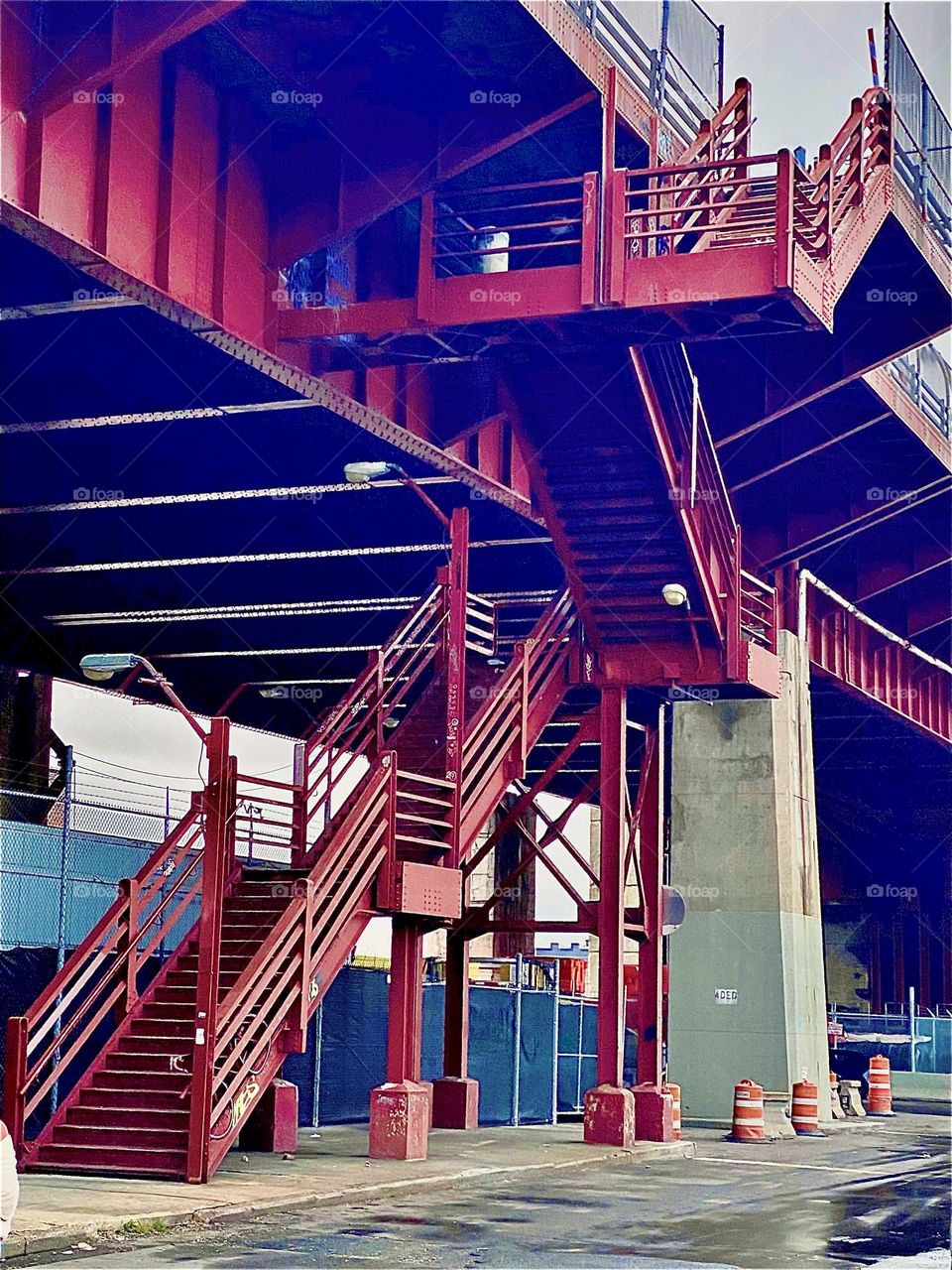 A red metal staircase leads up onto the pedestrian walkway over the Pulaski Bridge that spans the E River at Newtown Creek in LIC, Queens, NY and takes automobilists, bicyclists and walkers alike to Greenpoint, Bklyn. 2021. Hypnotic Productions