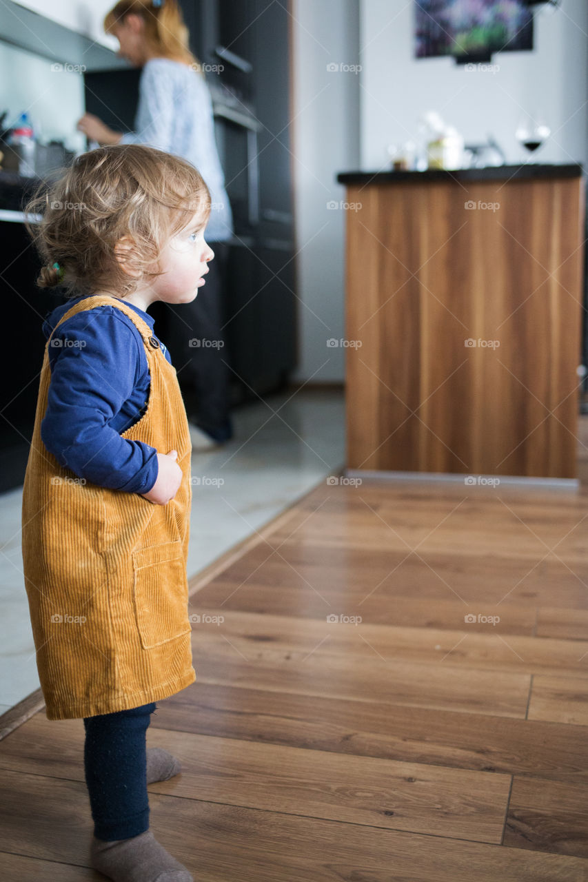 Little girl standing at home with mother in the background