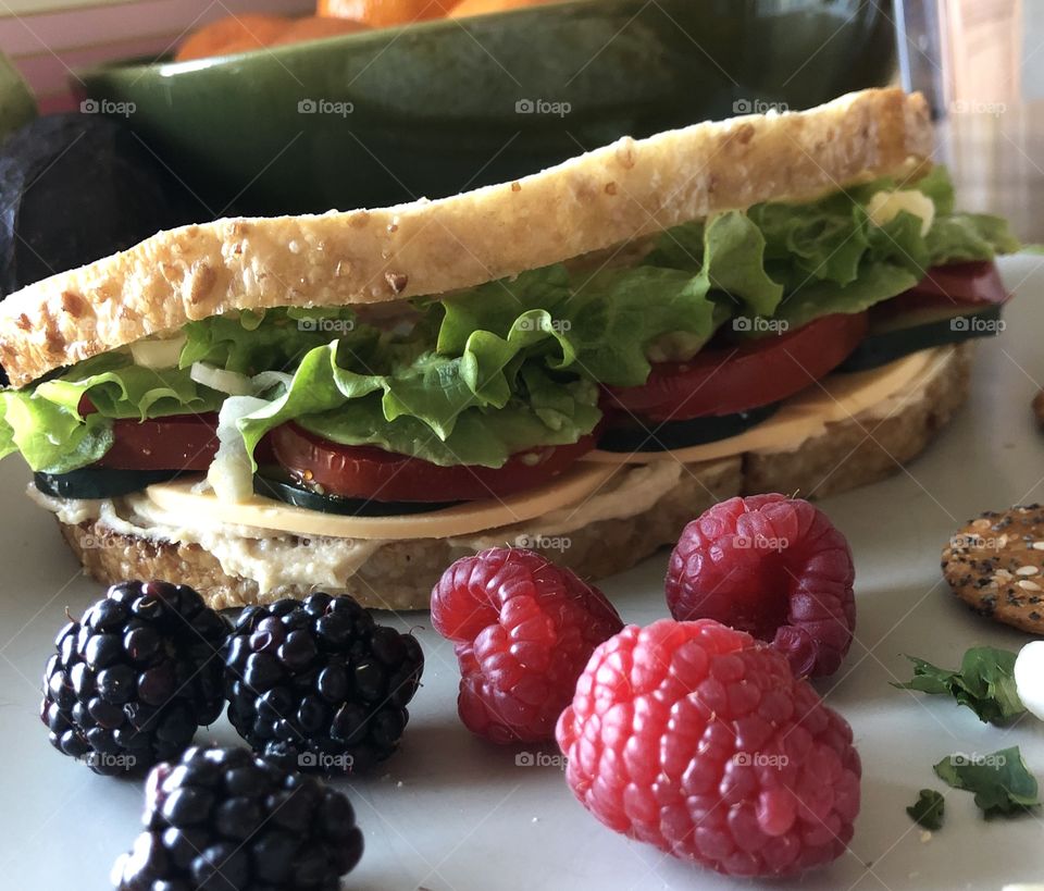 Cheese hummus green leaf lettuce red tomato cucumber avocado onion sandwich filling on toasted sourdough bread with raspberry and blackberry garnish