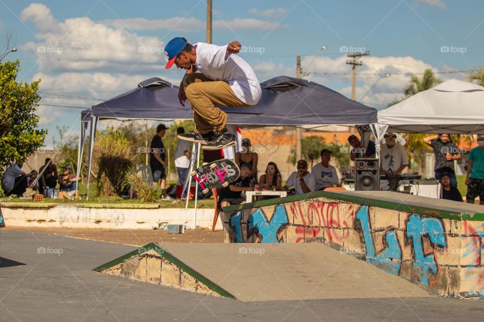 Skatista realizando manobra sobre obstáculo em pista de skate em dia ensolarado e bonito.