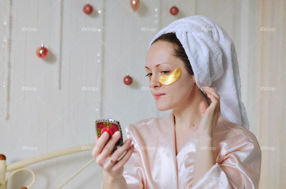 Young happy woman with a towel on head doing facial skin care procedures.   Beauty routine.  Cosmetic concept.  Patches at the face.