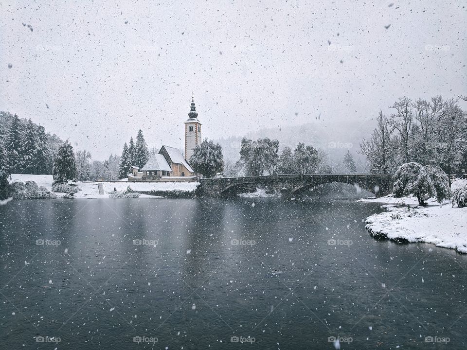 View of snowfall over the river and snow-covered Christmas trees in winter