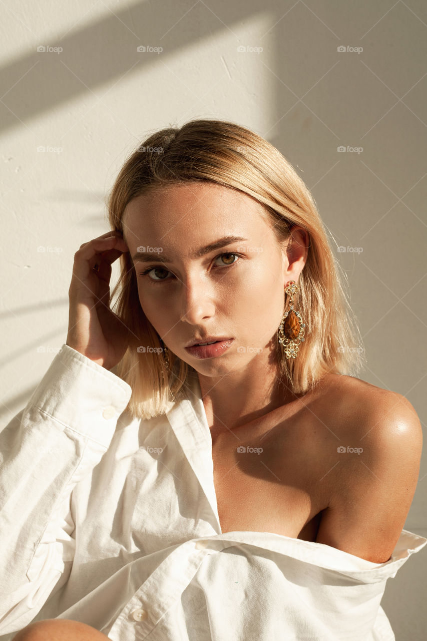 Beautiful blond woman in a white shirt. Portrait photo on a white background. Fashion photo. Jewelry. Short haircut. The woman looks into the camera.