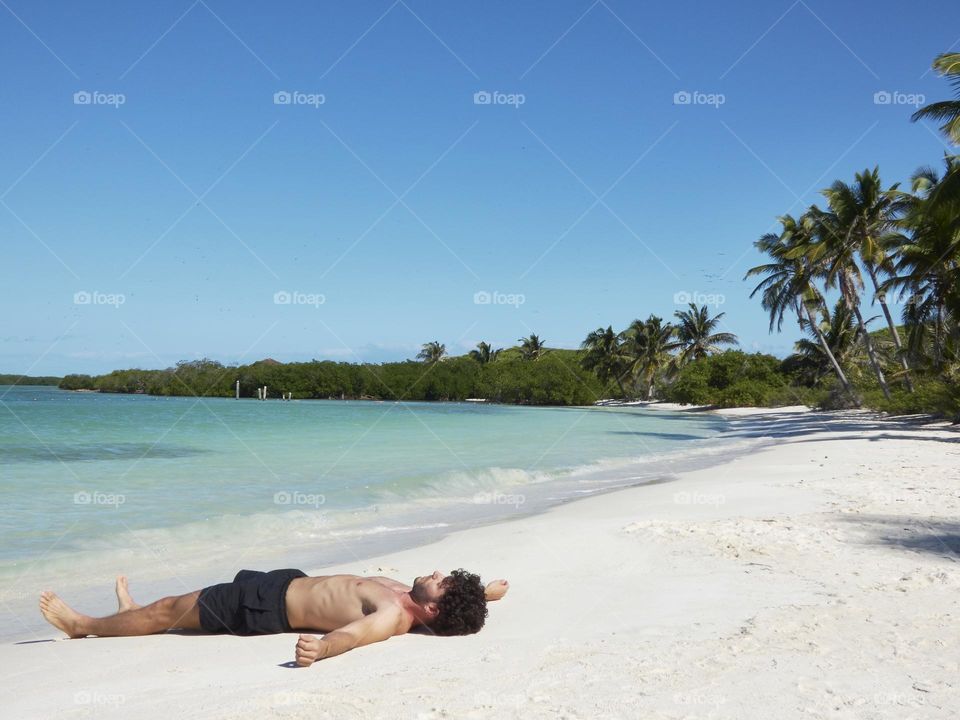 hombre acostado en una playa paradisíaca en un día totalmente soleado