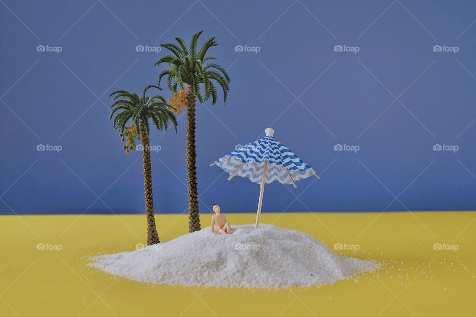 Close-up of miniature figure on sand and near miniature palm trees. 