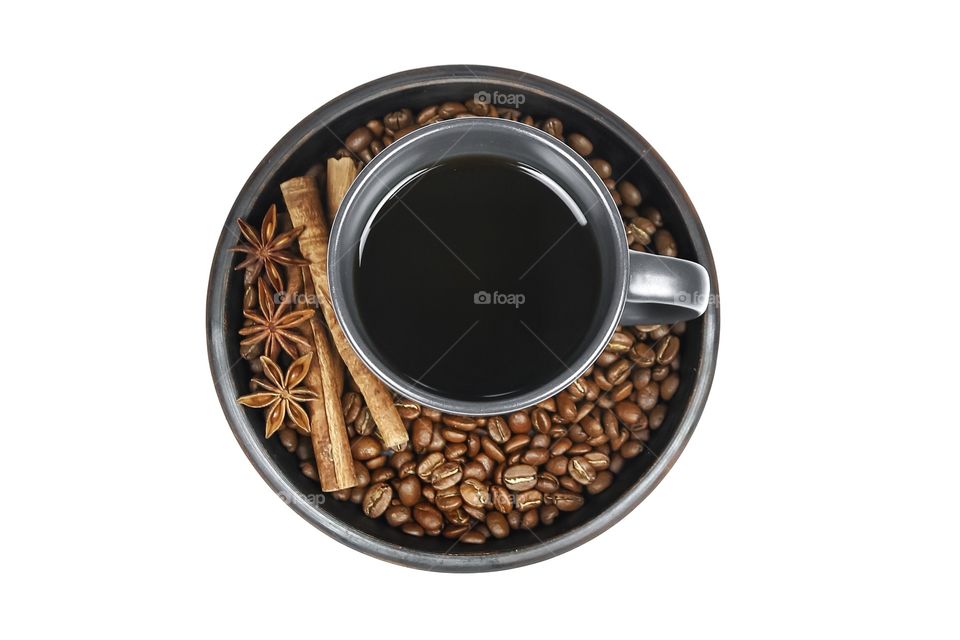 cup of black coffee on a plate with coffee beans and cinnamon on a white background