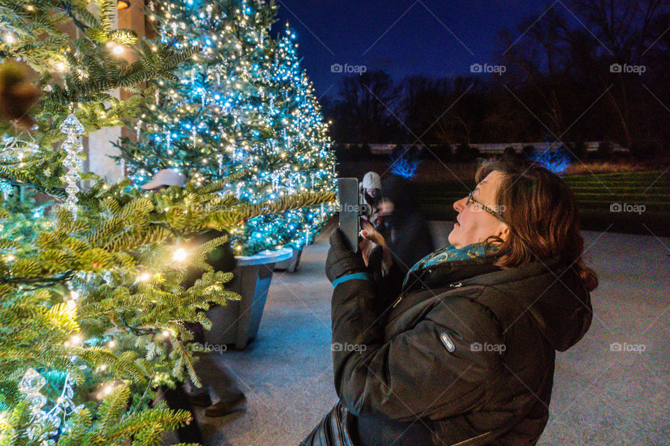 Woman taking photo of decorated Christmas tree with mobile phone