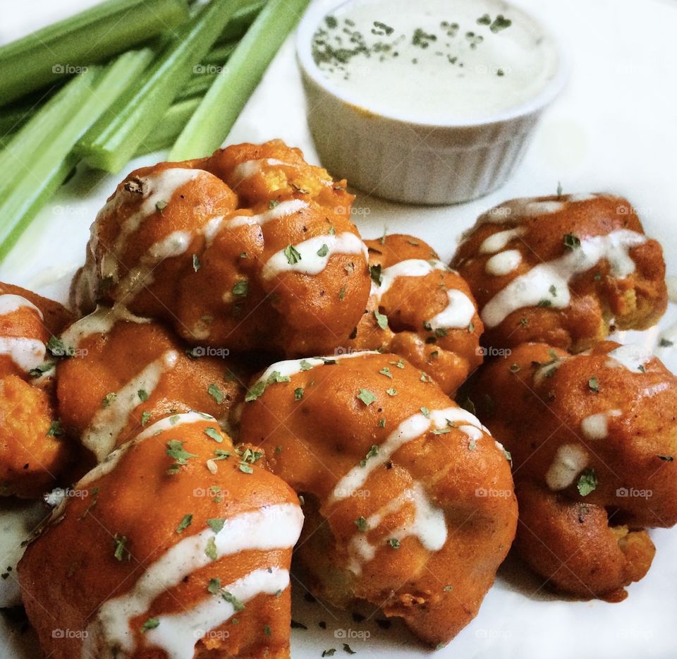 Buffalo cauliflower with creamy cashew cheese and celery sticks on a white plate.