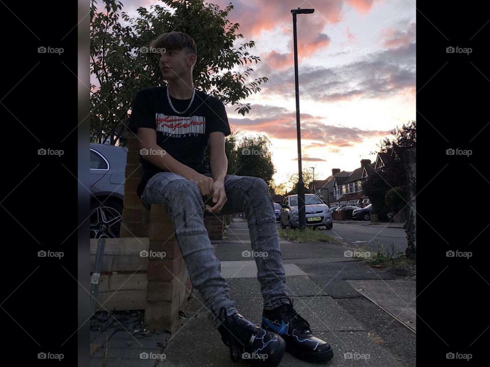 Picture of me sitting down with a nice sky in the background, relaxing setting. Wearing grey biker jeans a black shirt with a chain and black and blue lightning shoes.