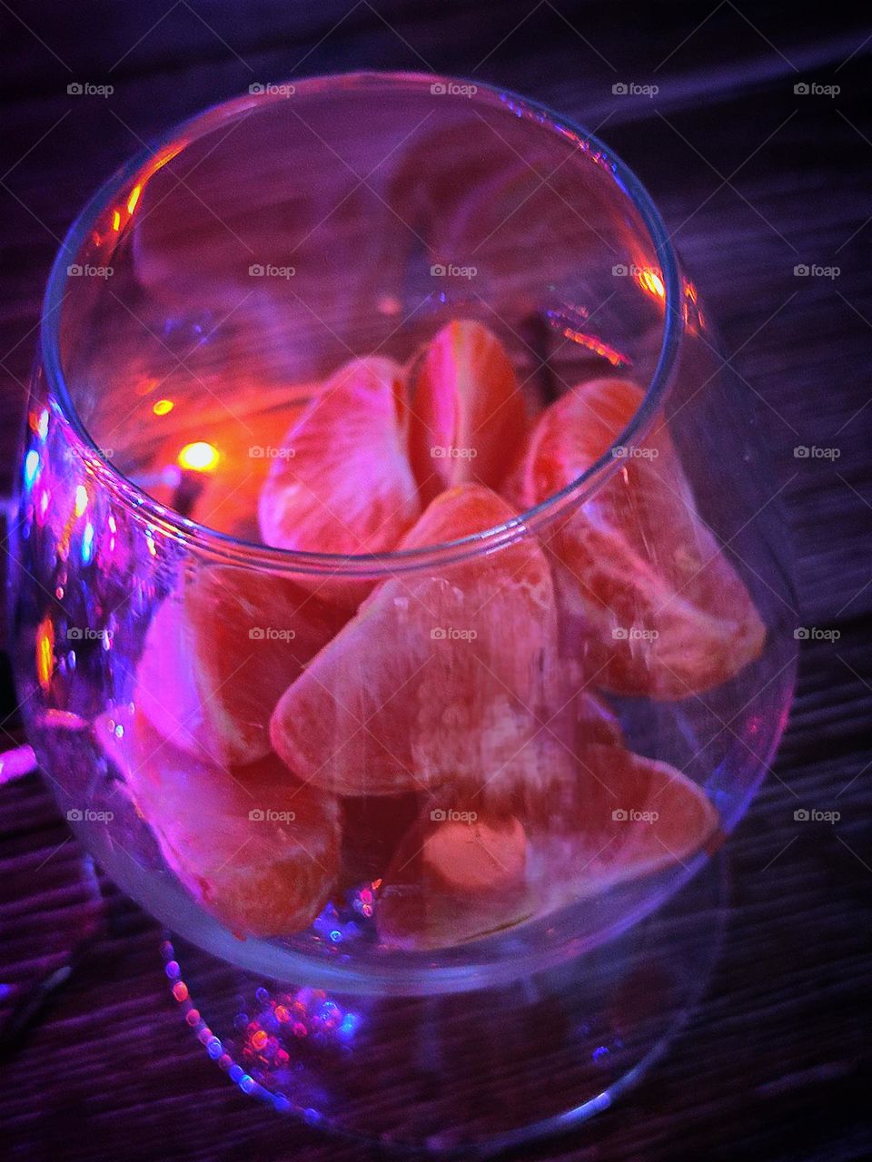 On a wooden background a glass with tangerine slices.  Illuminates the glass with light from the garland