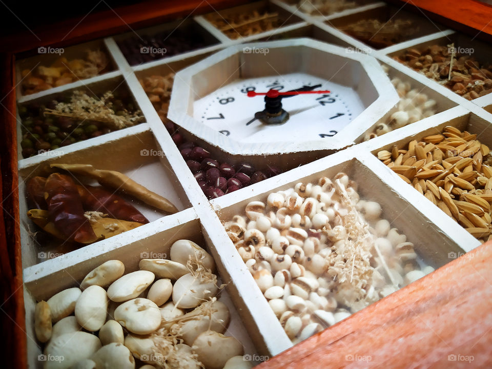 A clock divided into compartments containing seeds of various legumes