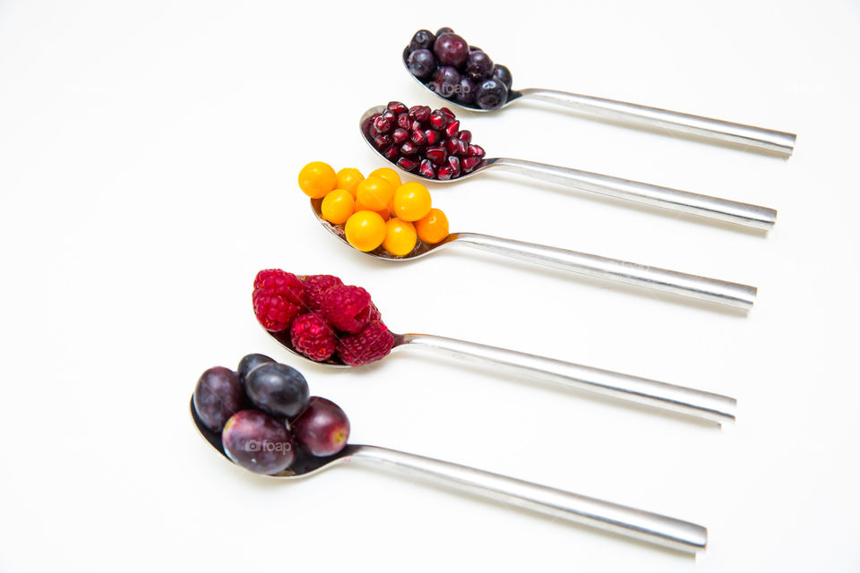 Different fresh and healthy summer fruits on silver spoons on a white background. Clean eating for health. Close up on a white background.