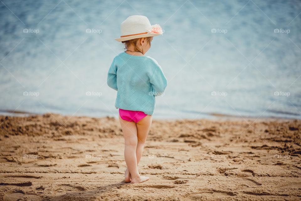 Little girl on lake coast at sunny evening.