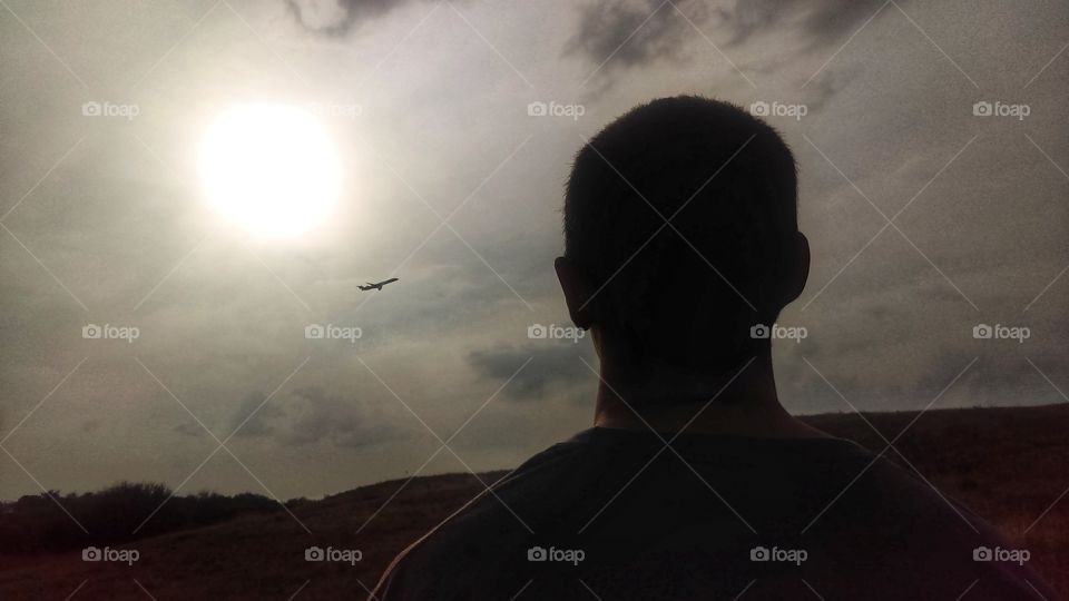 Silhouette of a man looking at a commercial plane flying near the sun