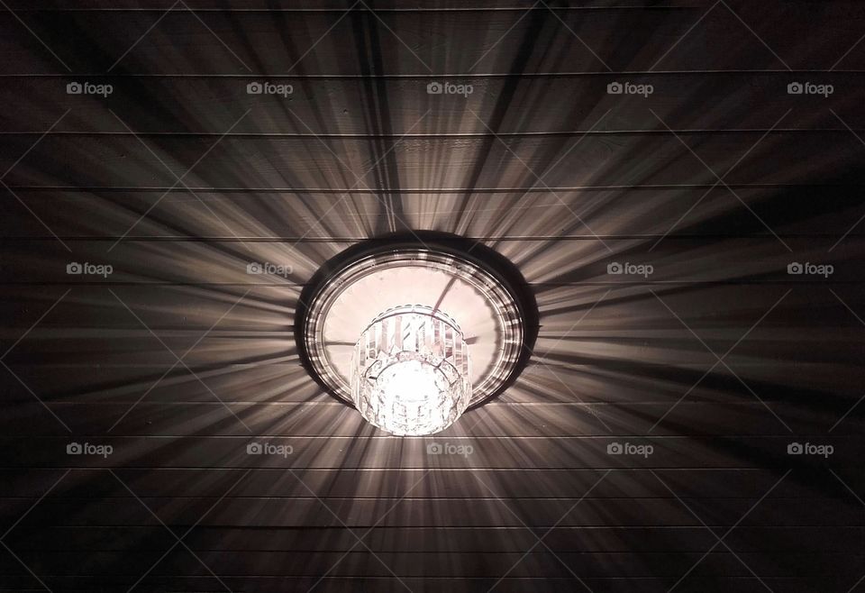 Crystal chandelier in the centre of a timber sheeted ceiling casting rays of light and shade across the surrounding surfaces