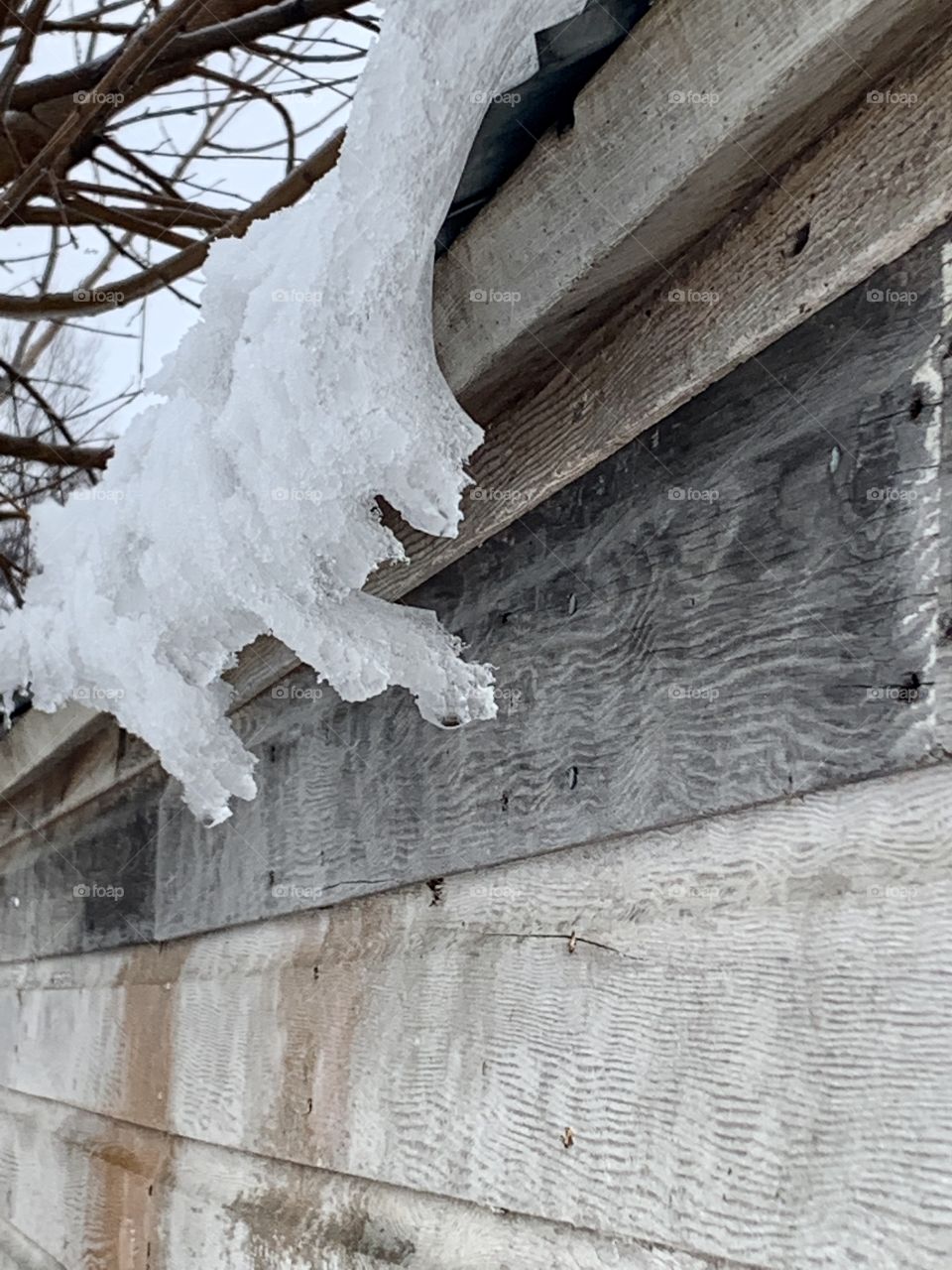 Snow and ice melting off of a metal roof of a rustic wooden structure 