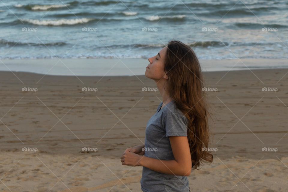 Young woman meditating on the beach and enjoying the fresh air 