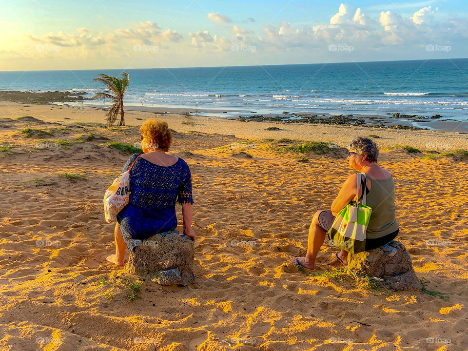 Two woman sitting in the beach waiting sunset 