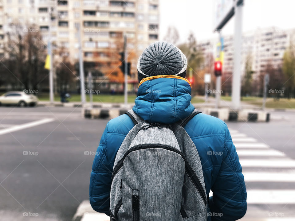 Young man with a backpack walking through the crosswalk in the autumn city 