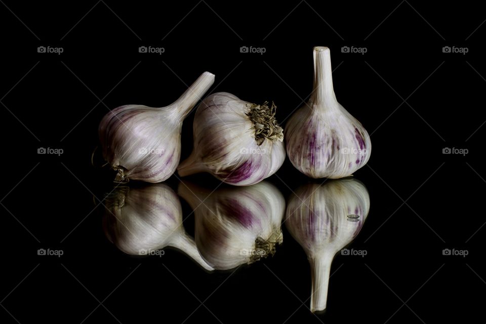 three heads of garlic with reflection on black background