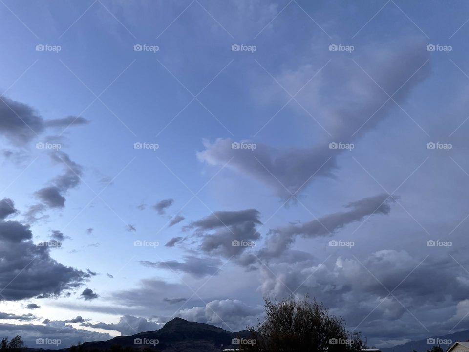 A photo of a mountain with several dark storm clouds above it with a tree in the frame. 