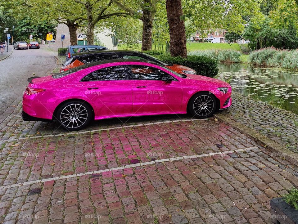 Foil wrapped Mercedes car in Barbie style, shining on the street with a bright pink glare