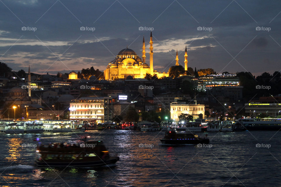 Boats cross the Golden Horn in Istanbul, Turkey  at night, with the Fatih mosque lit up in the background