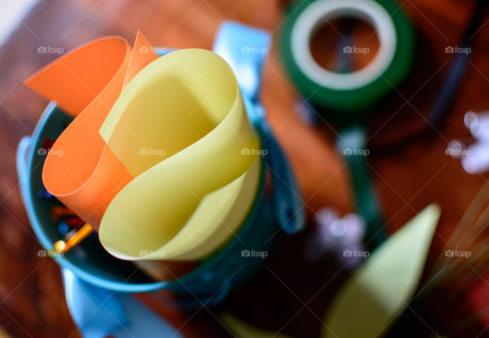 Colored paper and tape roll from High angle view of arts and crafts supply wooden desktop  work table with focus on  foreground of colored papers organized in bucket 