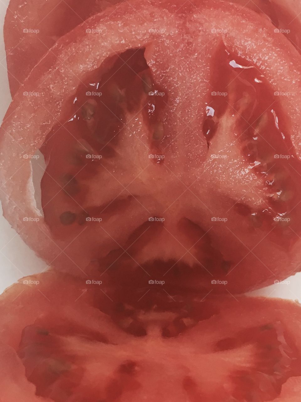 A slice of a red, juicy tomato sits on a White background. 
