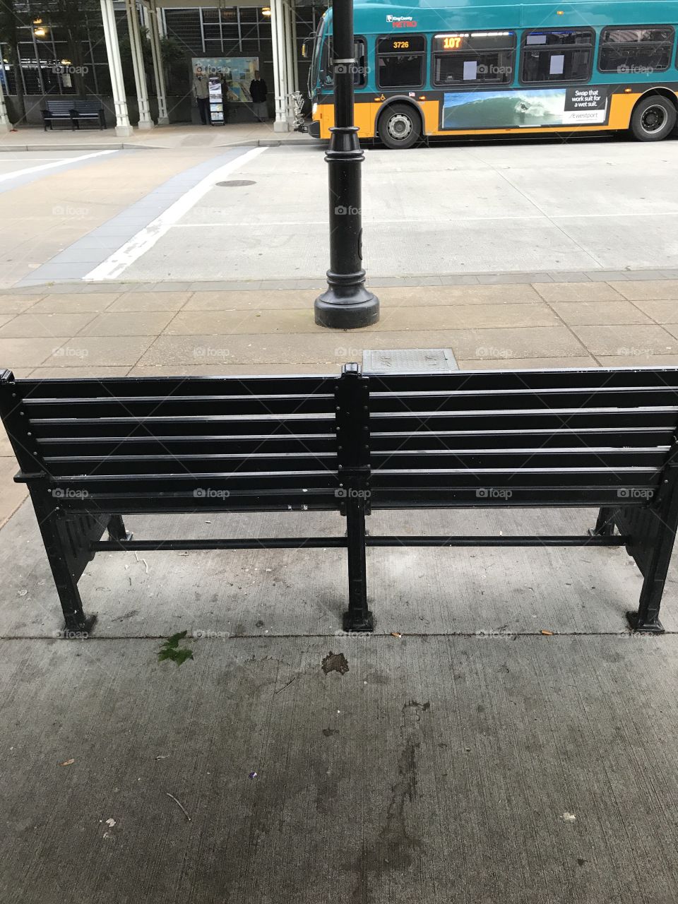 A bench at the bus stop with a street light directly in front of it.