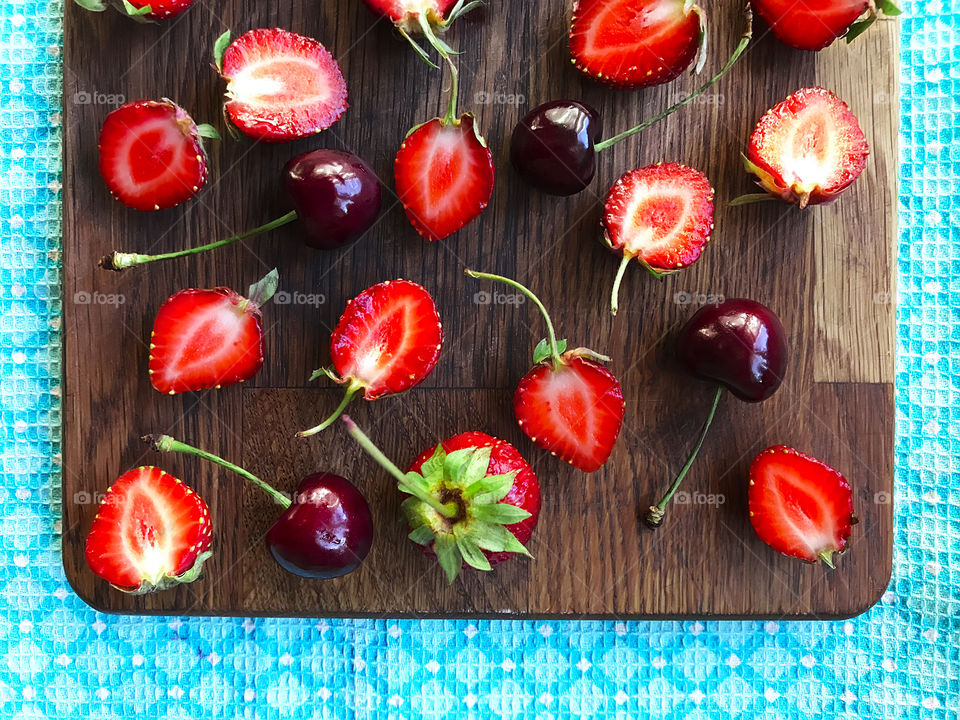 Strawberries and cherries on wooden board on blue textile background 