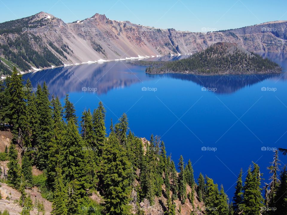 Wizard Island reflecting in the rich blue waters of Crater Lake in the forests of Southern Oregon on a sunny summer morning. 