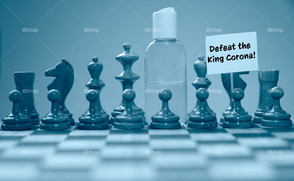 Coronavirus concept image chess pieces and hand sanitizer on chessboard illustrating global struggle against novel covid-19 outbreak with Defeat King Corona sign.