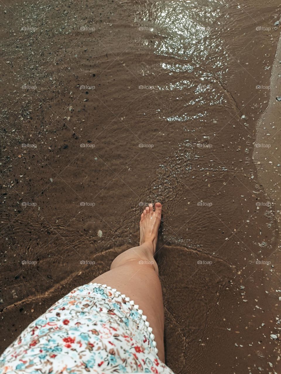 Close-up of the leg of a woman wearing a flowering short, taking a walk on the water edge of a beach