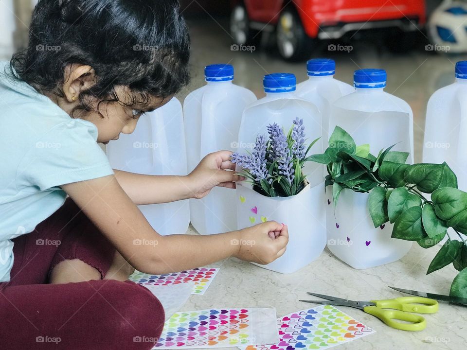 Girl pasting stickers on plastic milk bottles to make  a flower vases 