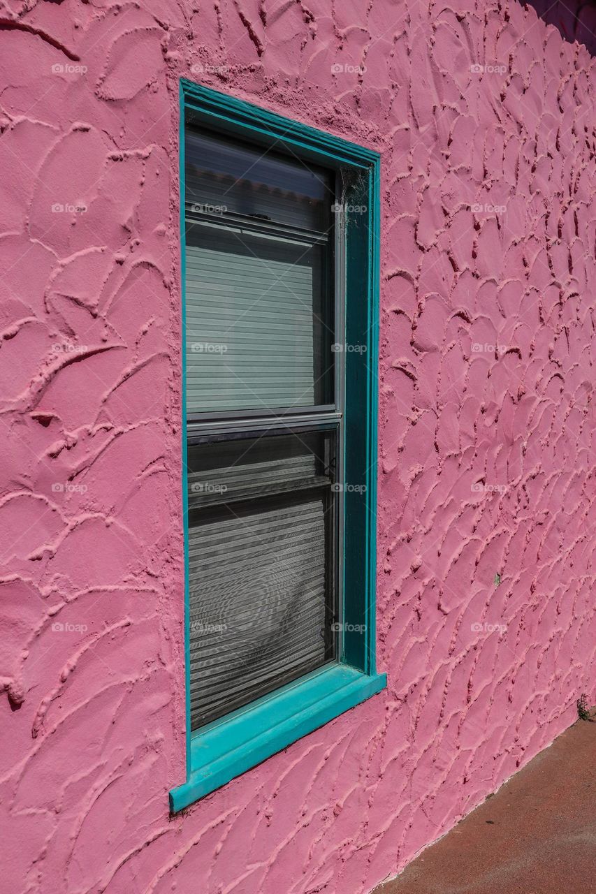Angled view of a pick stucco building with a window with turquoise trim, very Mediterranean in style 