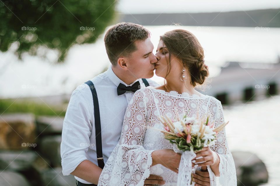 Happy newly married couple, smiling bride brunette young woman with the boho style bouquet with groom, close up portrait outdoors