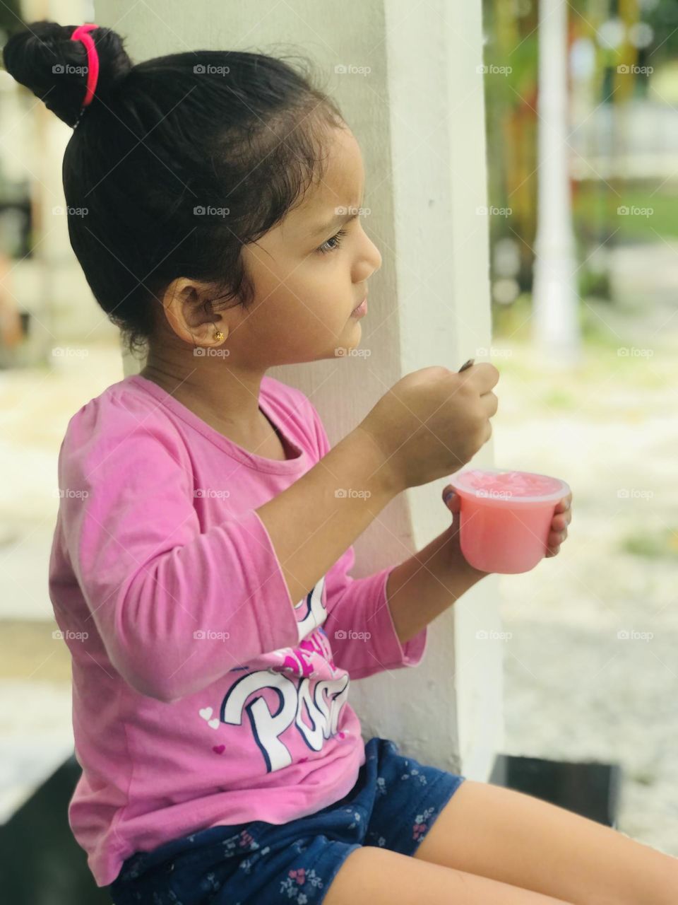 Baby girl eating pink colour strawberry pudding and enjoying and she wears pink dress on her