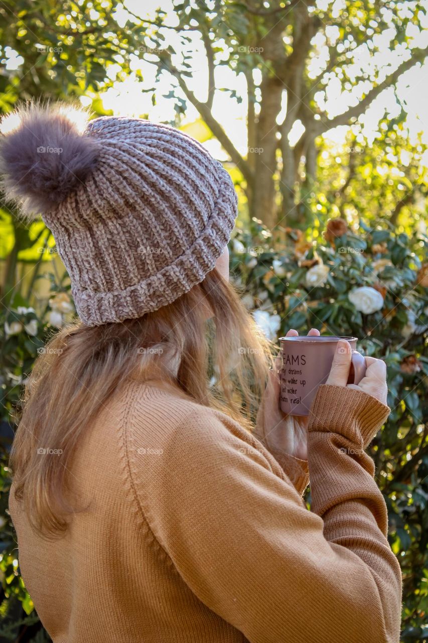 Woman standing with a cup of coffee on a cold morning and looking out at the garden