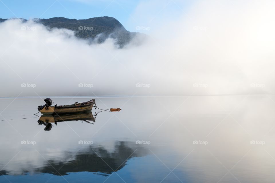 Small boat on a foggy sea. Small rowing boat on a foggy sea during sunrise. Mountain in the background is visible.