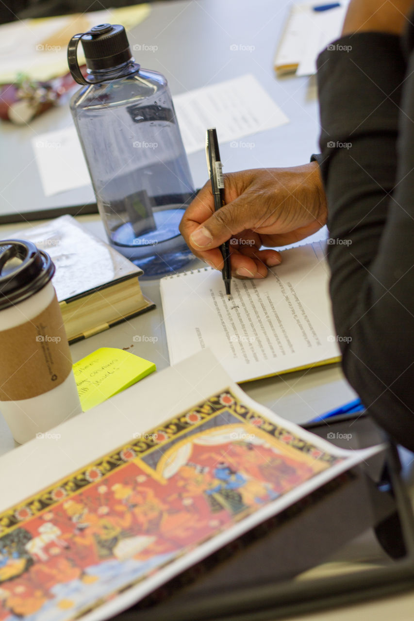 A man's hand writes in a book and plans an essay