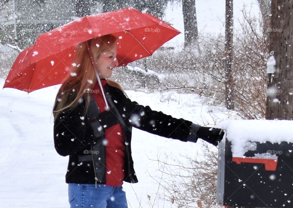 Red Totes umbrella held by a woman checking the mail in a snow storm