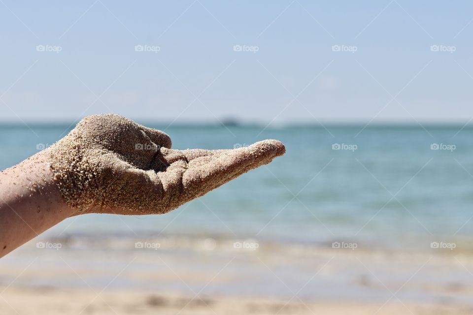 Summer in South Australia at beach, hand holding sand foreground ocean and beach blurred in background, copy text space background 