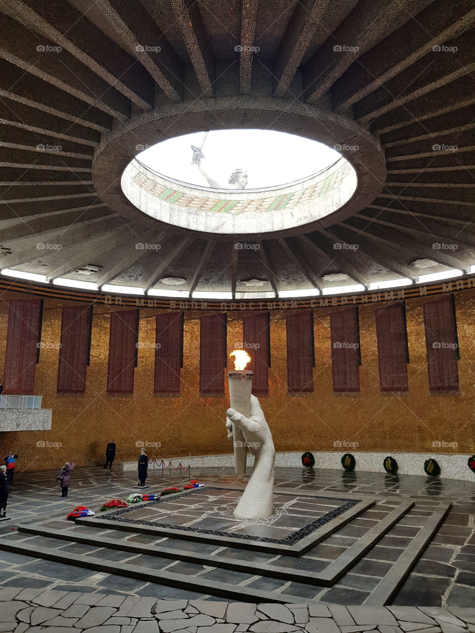 View on statue of victory through round opening in the ceiling of war memorial with hand holding eternal flame