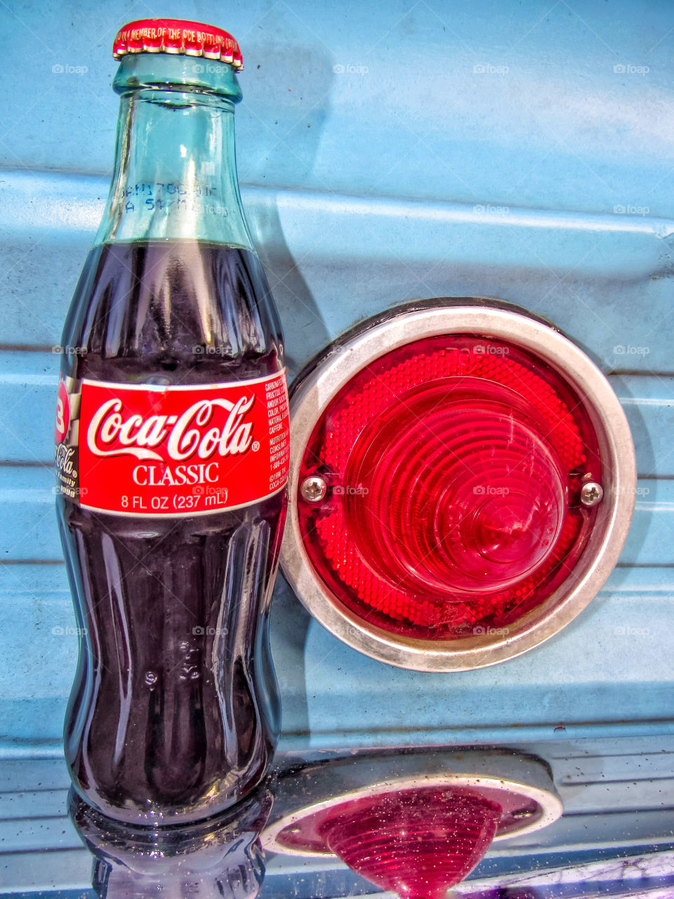 Coca-Cola bottle sitting on bumper of vintage car tail lights