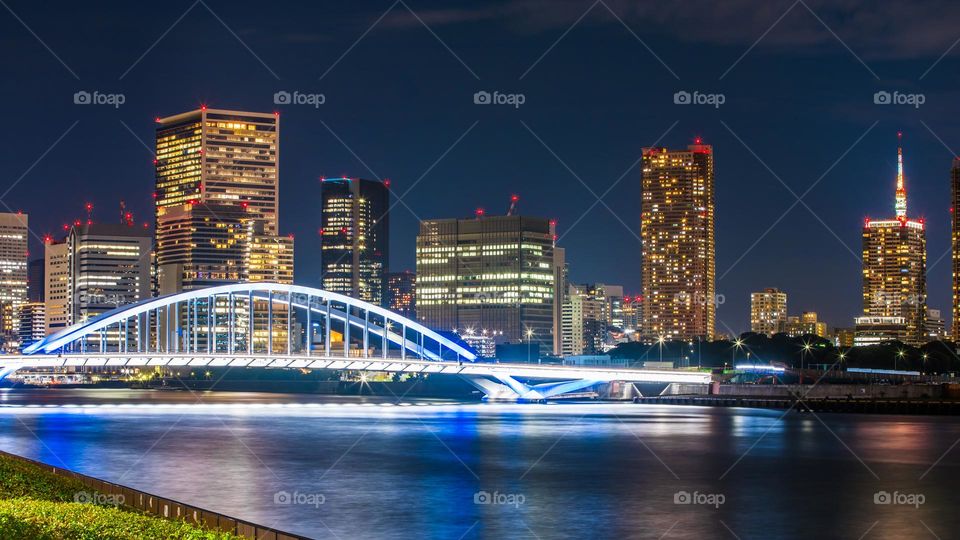 Tsukiji Ohashi Bridge in Tokyo, Japan and surrounding buildings at nighttime. Famous bridges span over the pictured Sumida River in Chuo Ku Ward City. Captured from the side of Kachidoki Bashi Bridge.